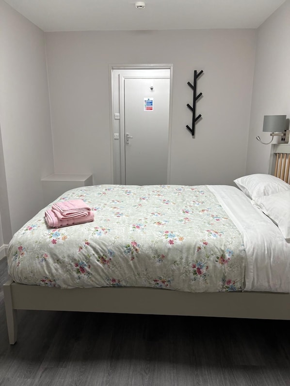 A bedroom with a bed, a door, a wall-mounted light, and a small shelf. - Central Hotel (Sutton-in-Ashfield)