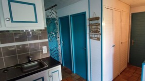 Cozinha com pia, armários e um objeto decorativo pendurado. Há portas azuis e uma placa com várias palavras.