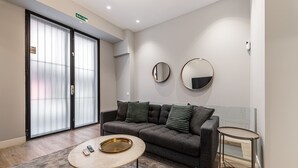 A modern living room with a grey sofa, two round mirrors, a small round table, and a sliding glass door with a 'SALIDA' sign. - Waou Essence III Tirso Molina - Corta Duración (Madrid)