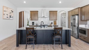 A modern kitchen with a central island, two bar stools, stainless steel appliances, and wooden cabinetry.