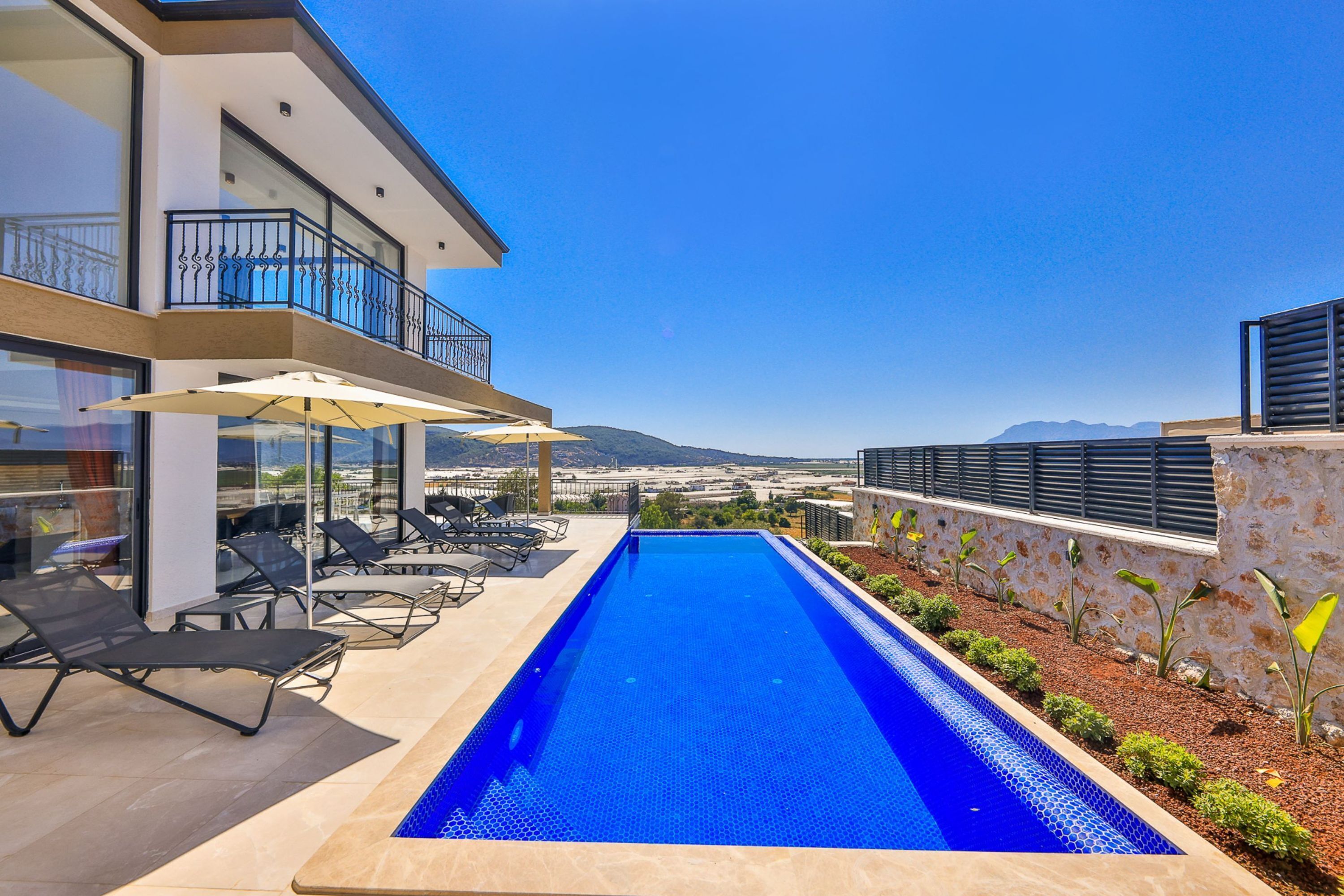 Un área de piscina moderna con vistas despejadas a las montañas, tumbonas y barandilla de cristal.