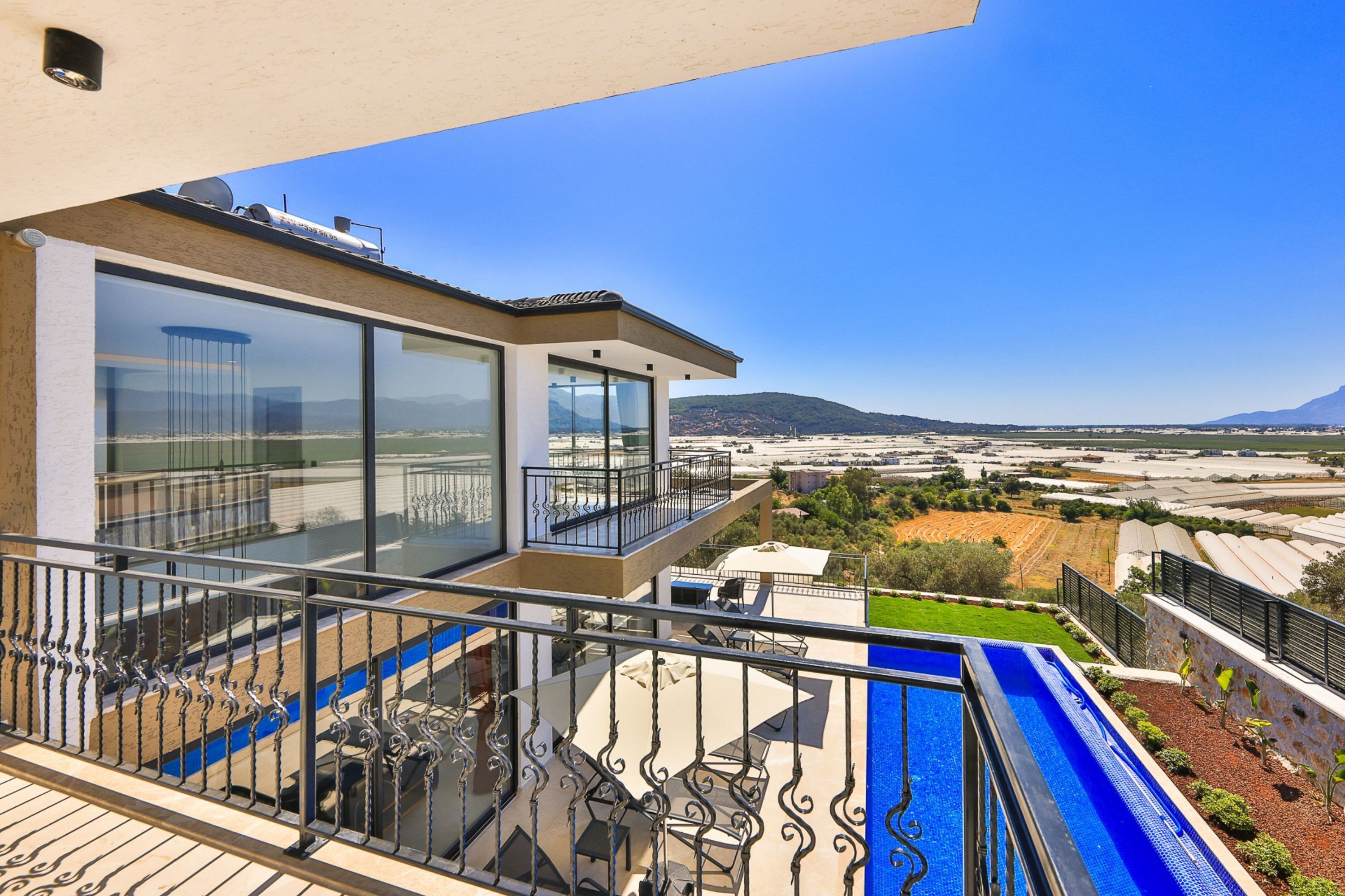 A modern balcony with a glass railing overlooking a swimming pool and a scenic view of a coastal landscape.