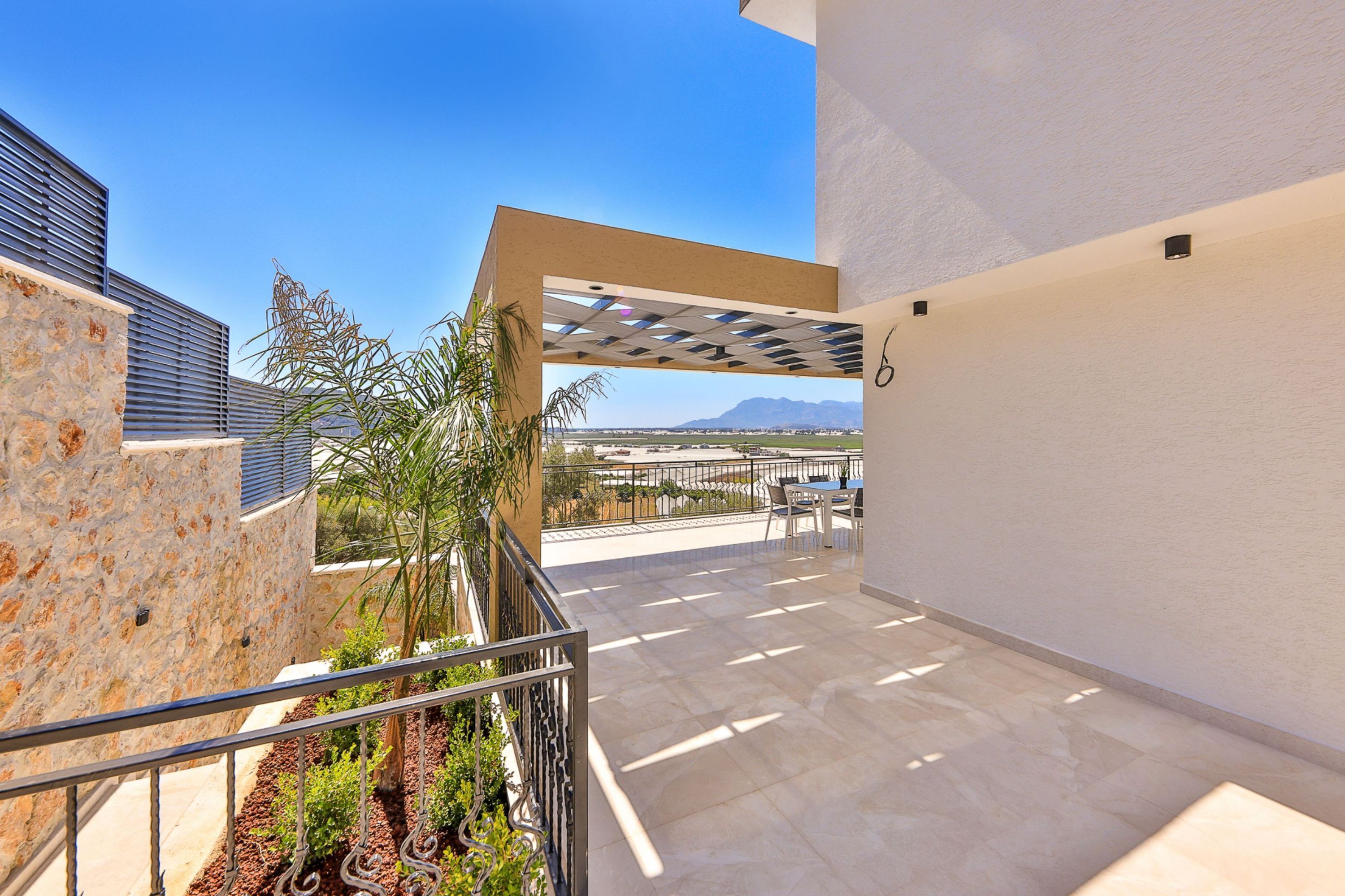 A modern outdoor patio with a pergola, stone walls, and a view of distant mountains.