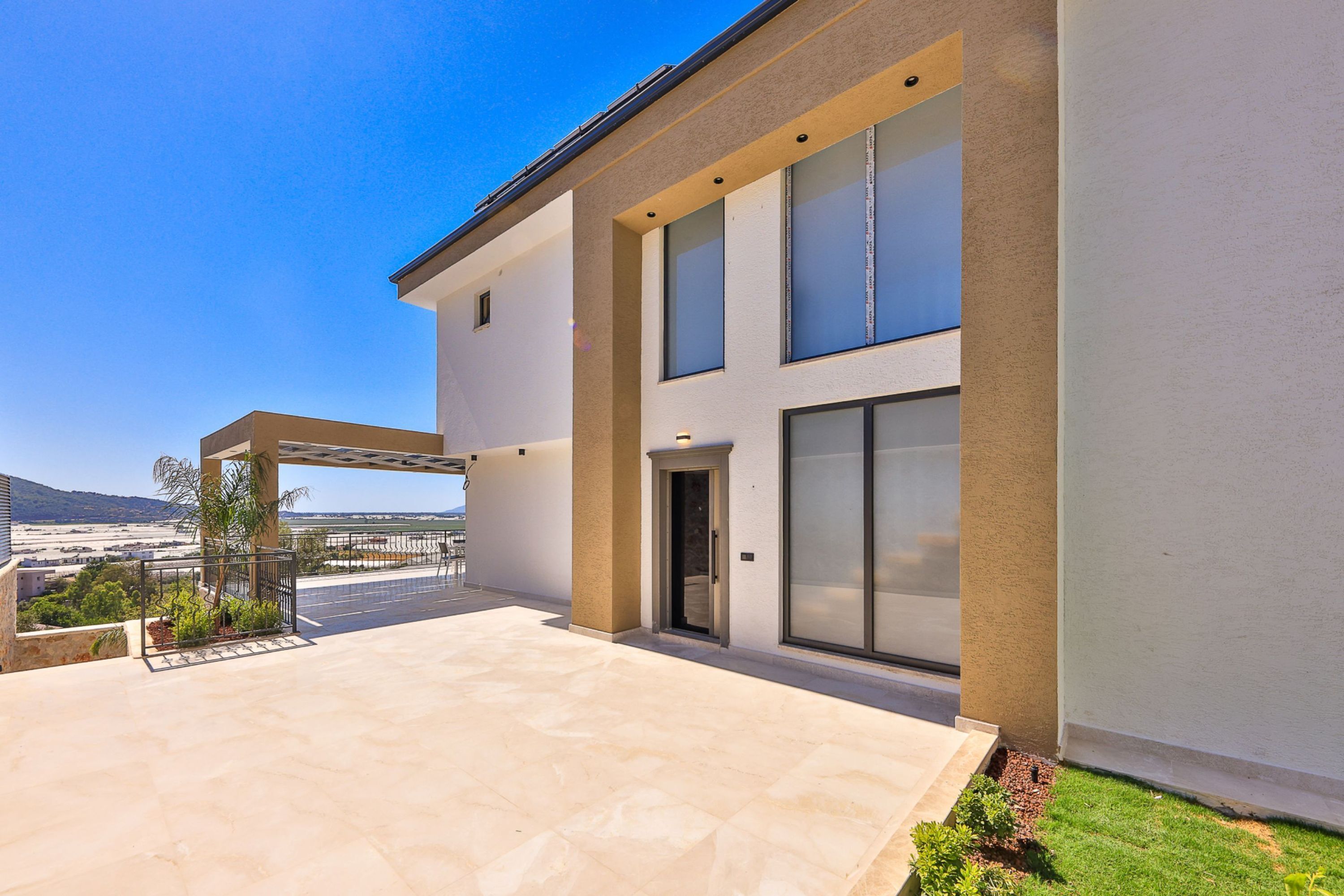 A modern two-story house with a covered patio, large windows, and a view of the landscape.