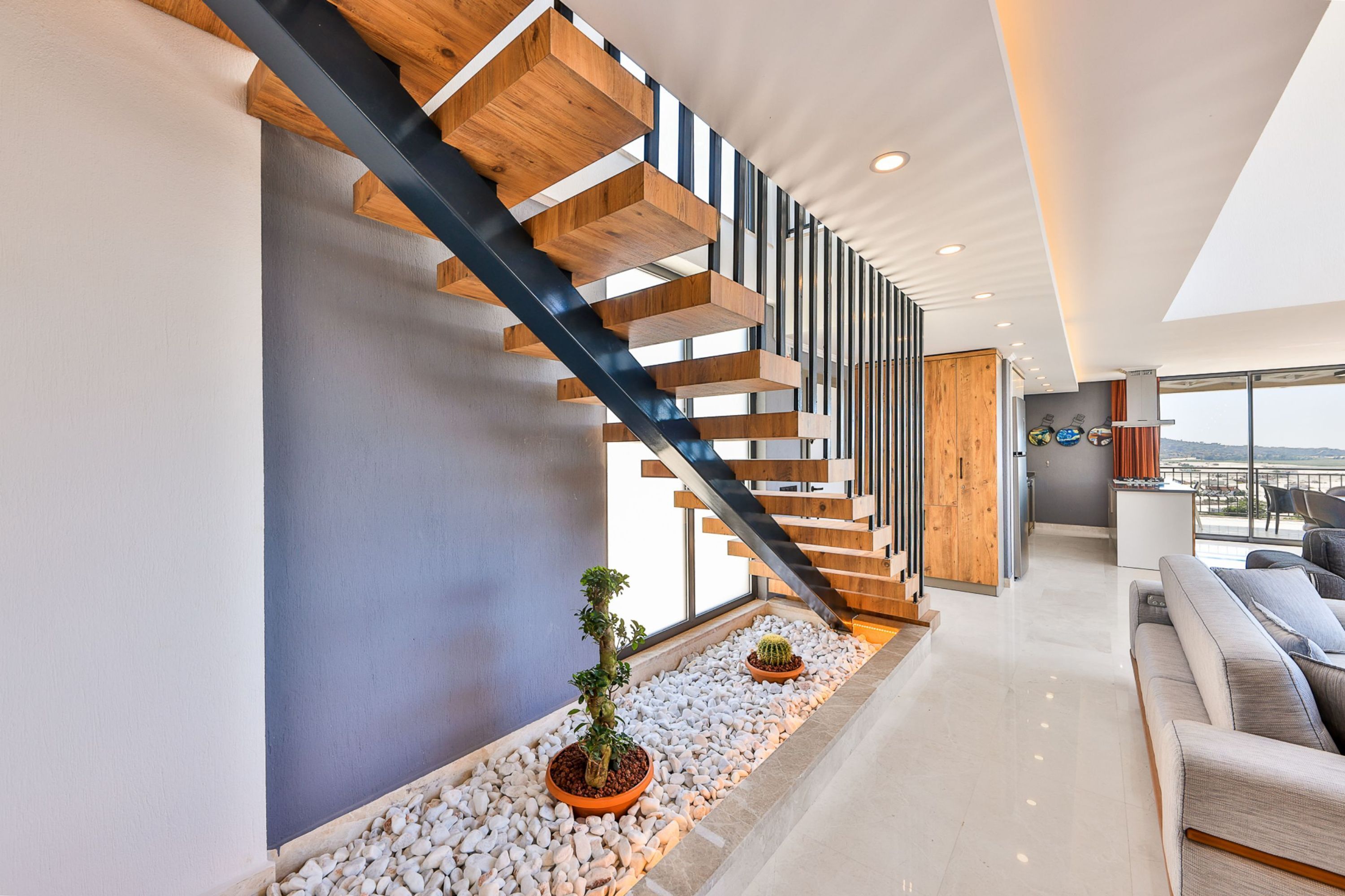 Een modern interieur met een houten trap, een zithoek met een bank en uitzicht door grote ramen.