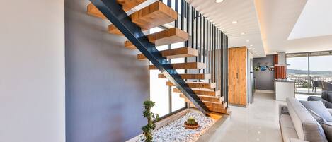Een modern interieur met een houten trap, een zithoek met een bank en uitzicht door grote ramen.