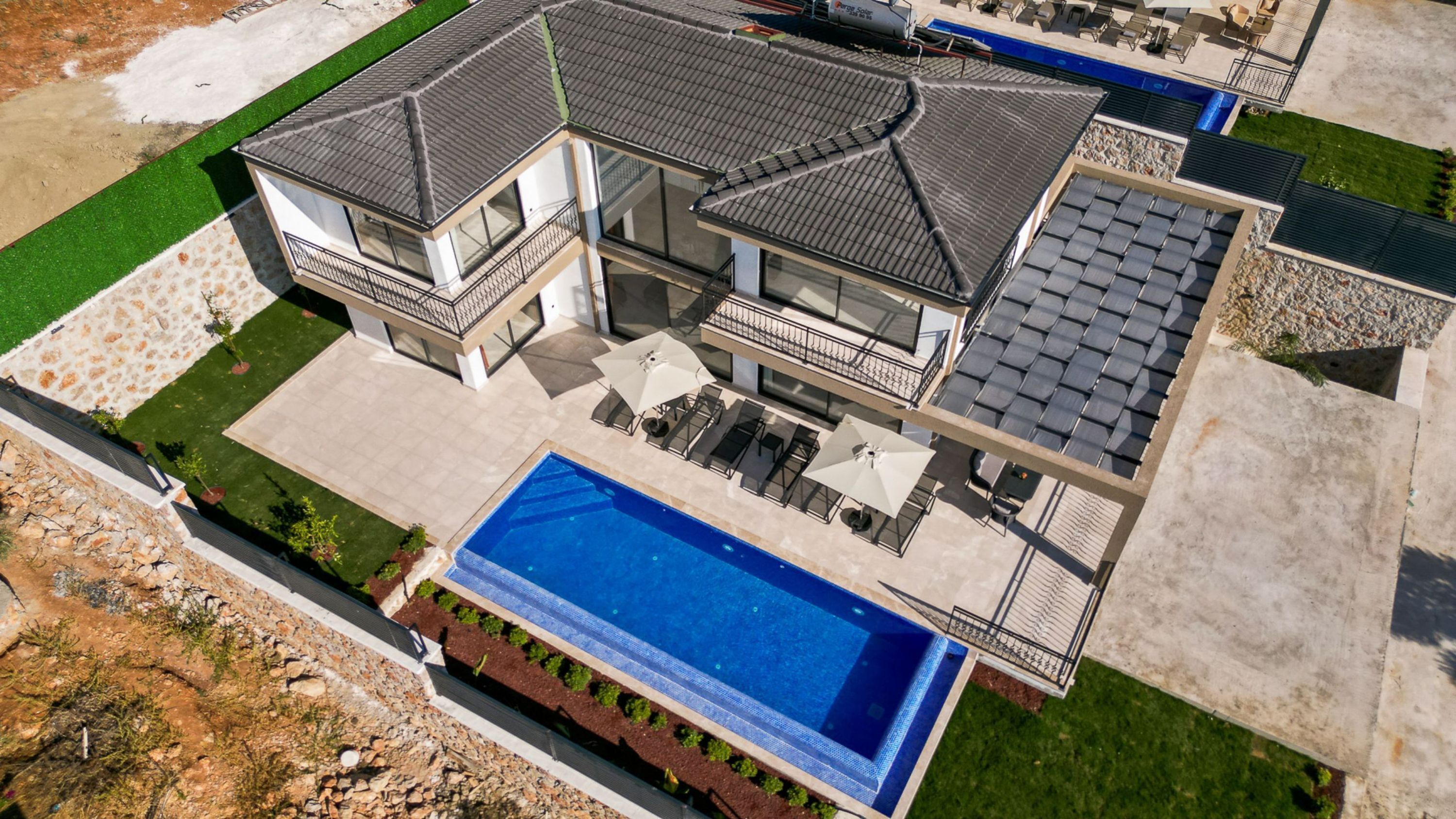 A modern two-story house with a large swimming pool, multiple balconies, and a covered patio area.