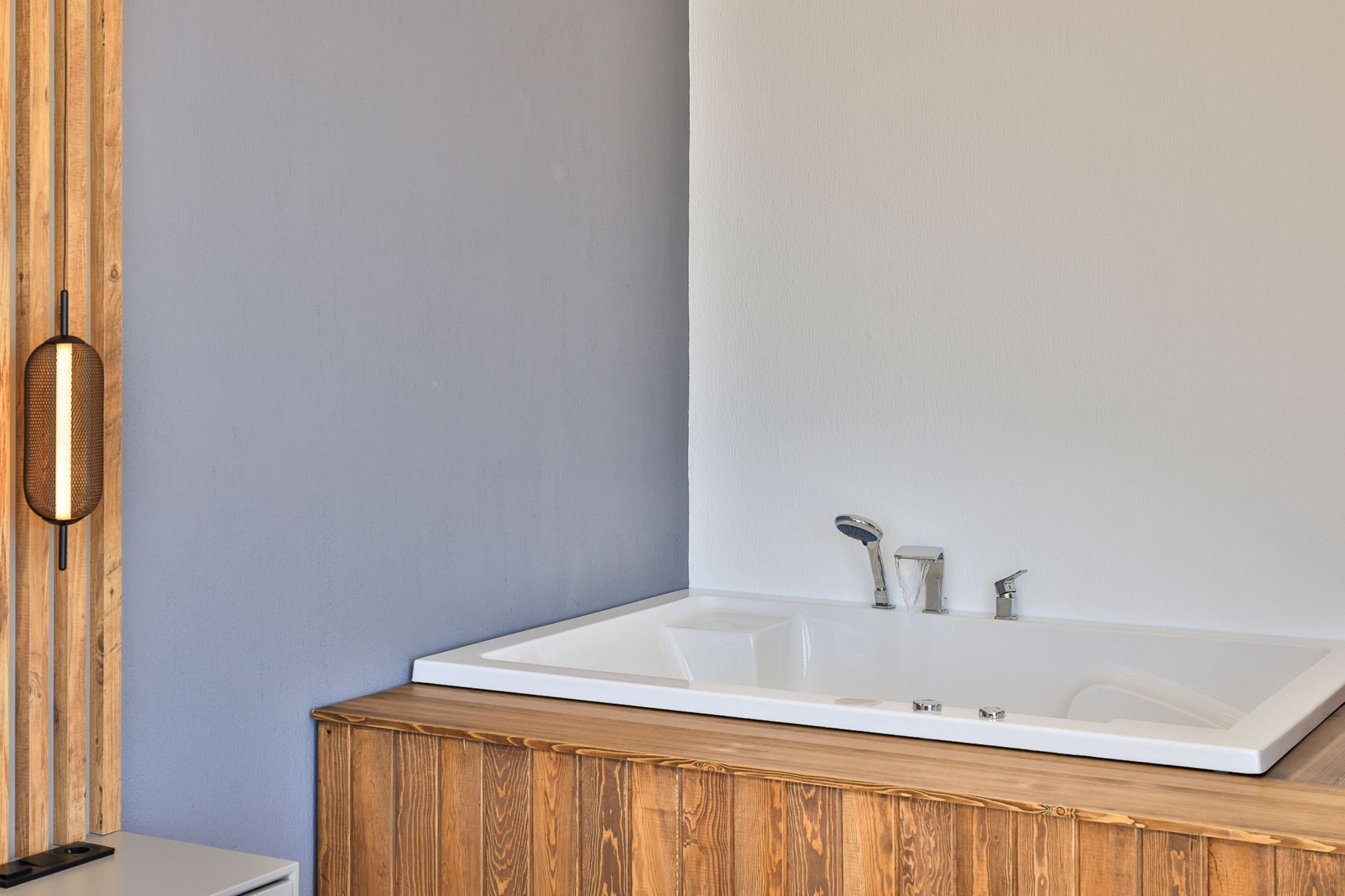 A modern bathroom with a large bathtub, wooden vanity, and a wall-mounted light fixture.