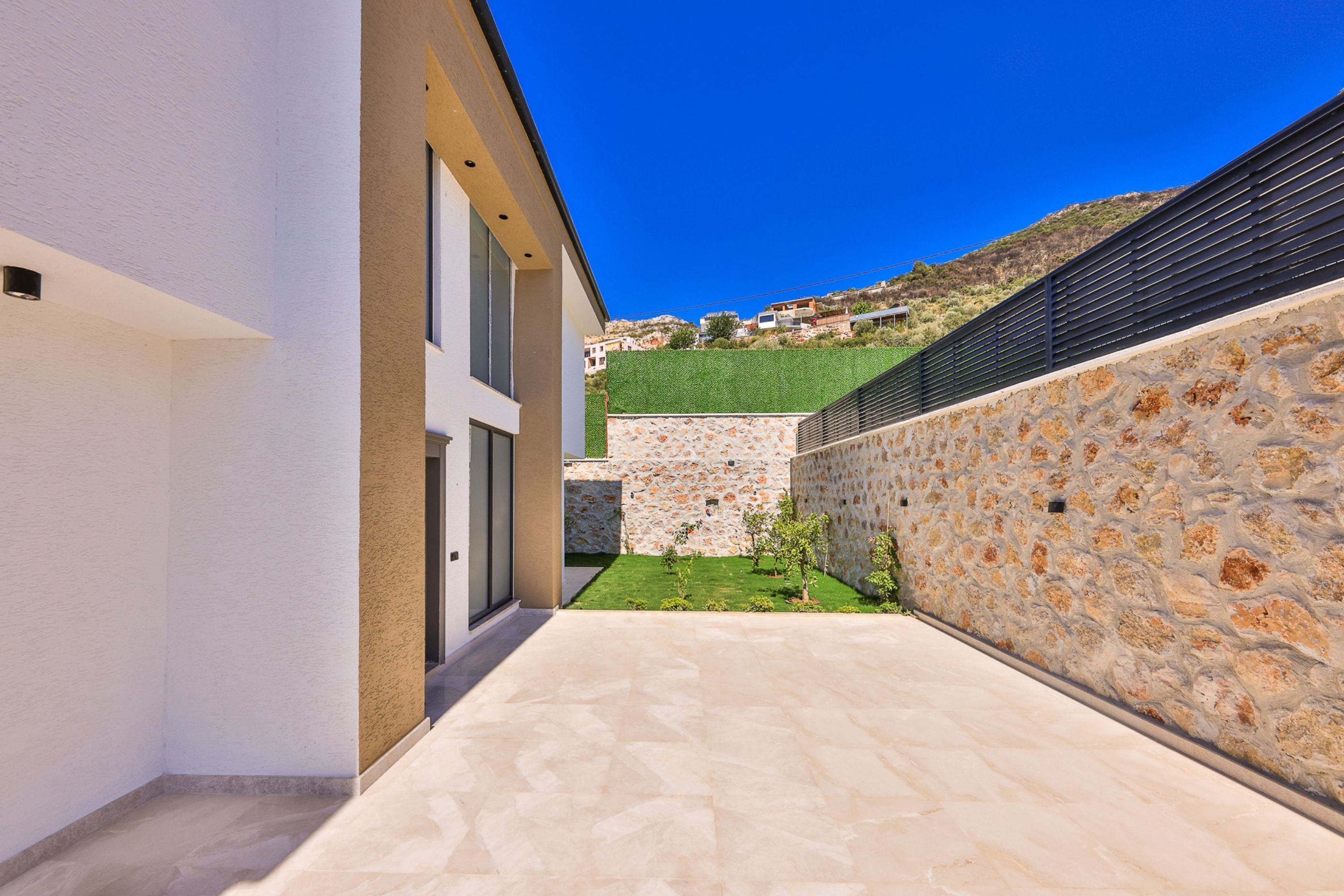A modern building with a stone wall, a small garden, and a clear blue sky.