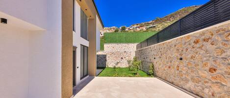 A modern building with a stone wall, a small garden, and a clear blue sky.