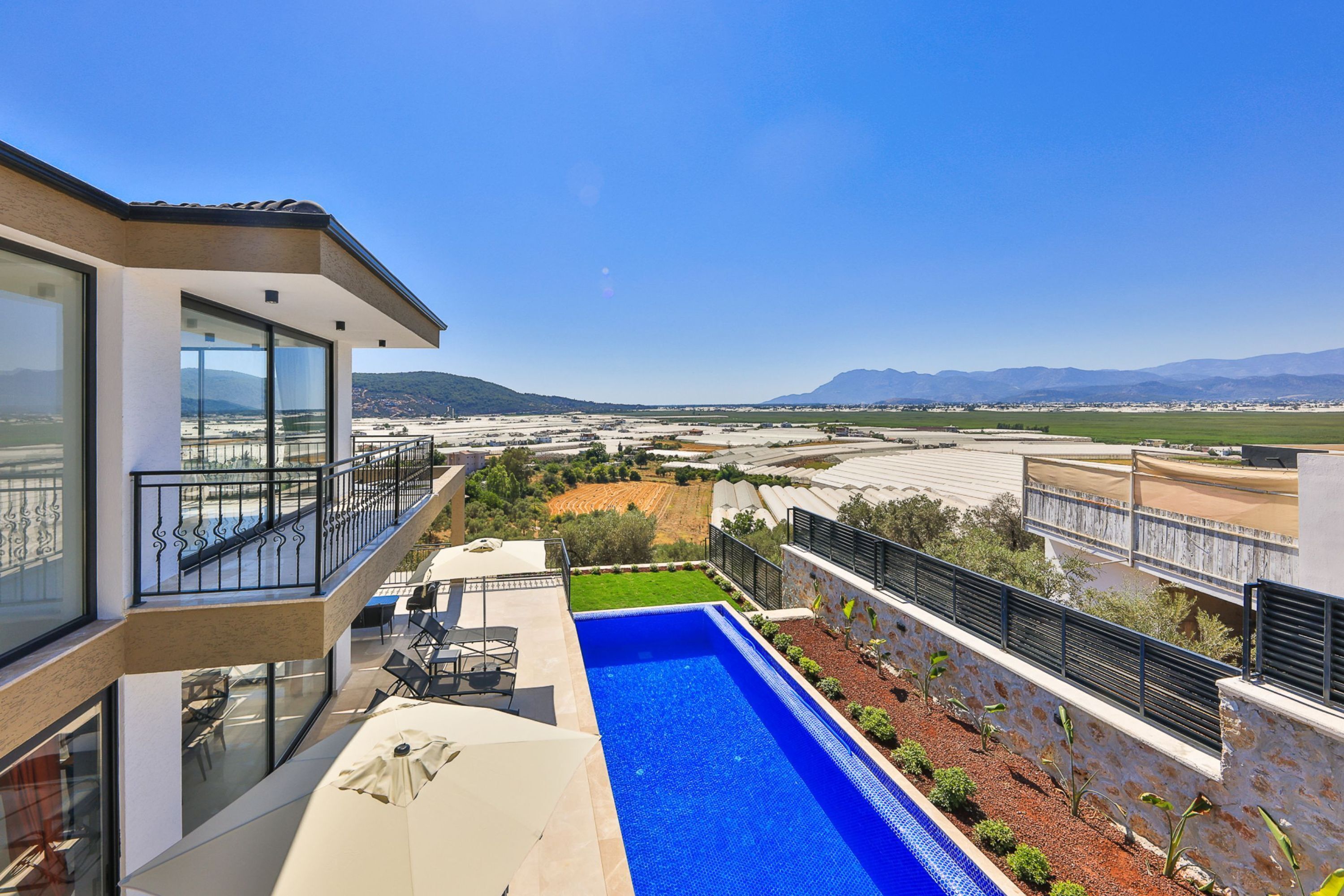 A modern house with a large balcony, a swimming pool, and a view of distant mountains and fields.