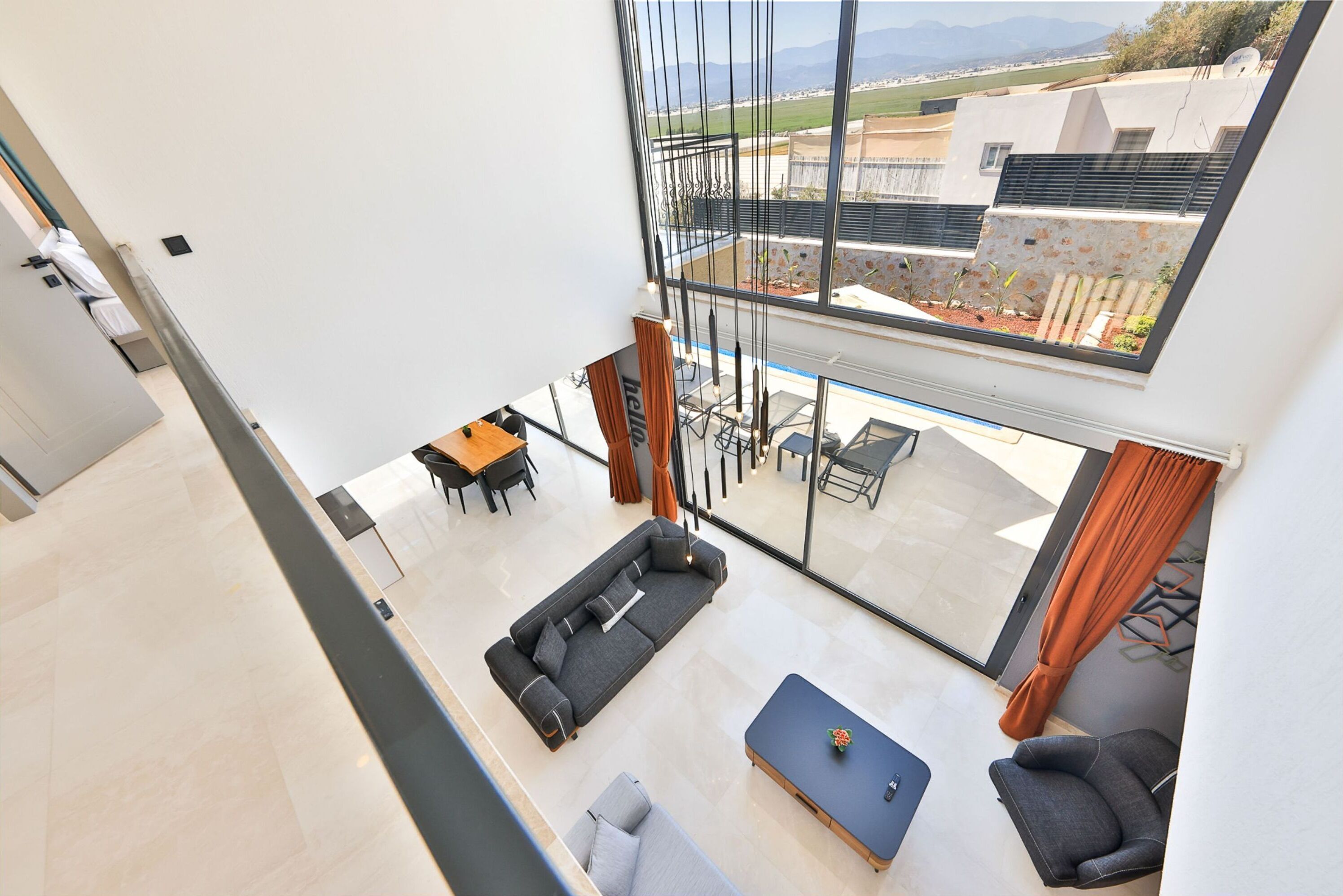 Un salon moderne avec un canapé d’angle, une table basse et un coin repas comprenant une table et des chaises. Une grande fenêtre offre une vue sur l’extérieur.