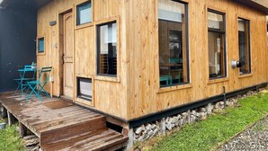 Eine Holzhütte mit einer Terrasse, großen Fenstern und einer Tür.