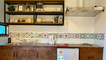 A kitchen with wooden cabinets, a stainless steel sink, and a refrigerator. There are shelves above the sink holding various kitchen items and a small chalkboard with a message.