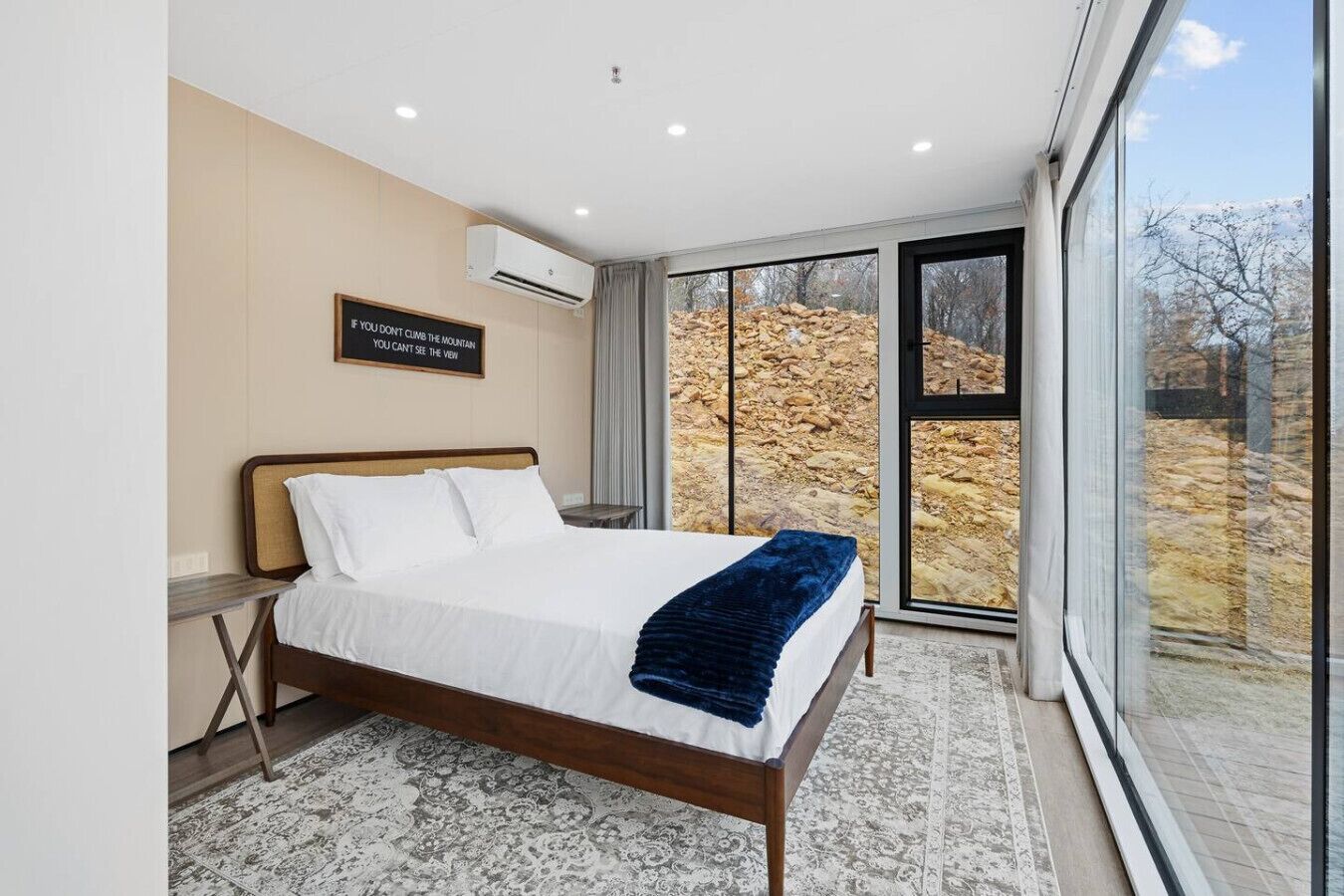 A modern bedroom with a large bed, a view of a rocky landscape through a glass door, and a motivational quote on the wall.