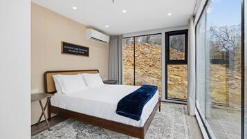 A modern bedroom with a large bed, a view of a rocky landscape through a glass door, and a motivational quote on the wall.