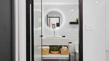 Un bany modern amb porta de vidre, un lavabo blanc, un mirall rodó i una planta petita.