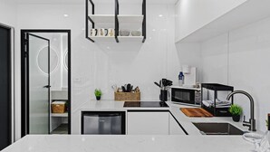 A modern kitchen with white cabinetry, a built-in microwave, a coffee maker, and a black hanging shelf.