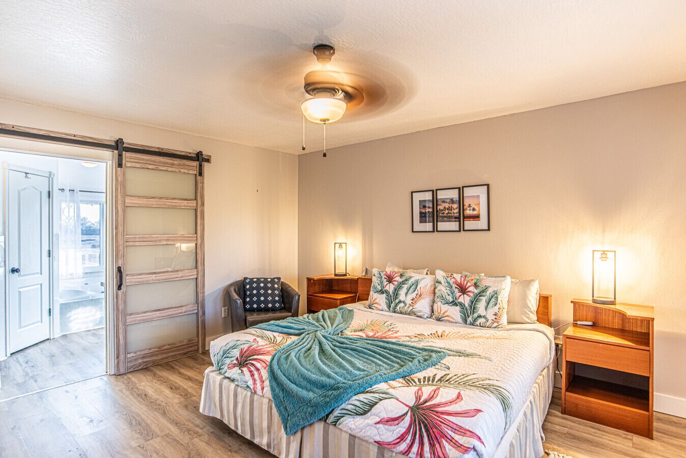 A bedroom with a bed, nightstands, a chair, a ceiling fan, and a sliding glass door.