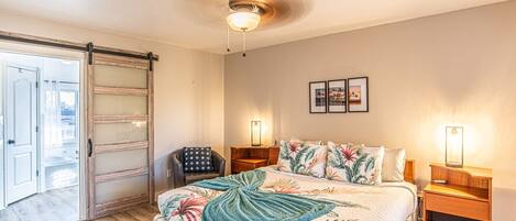 A bedroom with a bed, nightstands, a chair, a ceiling fan, and a sliding glass door.