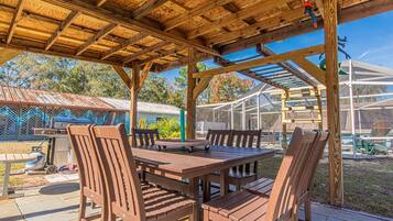 A covered outdoor patio with a wooden table and chairs, a grill, and a transparent enclosure in the background.
