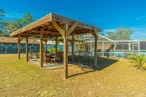 A wooden gazebo with a swing, a pool, and a covered patio area.