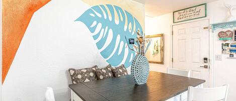 A dining area with a dark wooden table, white chairs, and a decorative wall with a large leaf pattern.