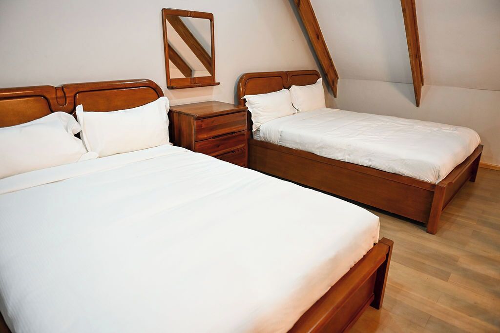 Une chambre avec deux lits en bois, chacun agrémenté de draps blancs, une table de chevet en bois et un miroir.