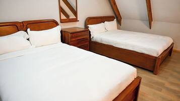 Une chambre avec deux lits en bois, chacun agrémenté de draps blancs, une table de chevet en bois et un miroir.