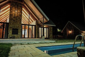 Un edificio de piedra con amplios ventanales y una piscina al frente.