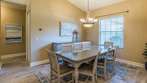 A dining area with a glass table, wooden chairs, a chandelier, and a window with blinds. - PerfectPointeLakehouse|PvtDock|Kayaks|8ppl|Firepit|ScreenedPatio (Hernando)