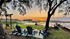 A lakeside seating area with Adirondack chairs and a wooden deck overlooking the water. - PerfectPointeLakehouse|PvtDock|Kayaks|8ppl|Firepit|ScreenedPatio (Hernando)
