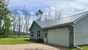 Une maison de plain-pied avec un garage, entourée d’une cour verdoyante et d’arbres.