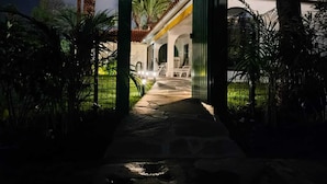 Un sentiero conduce a un edificio con tetto a tegole e colonne, circondato da palme e vegetazione.