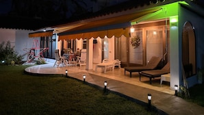 Una casa moderna con patio coperto, area salotto esterna e ingresso ben illuminato.