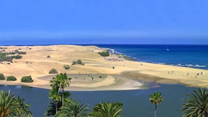 Paesaggio costiero con dune di sabbia, una spiaggia e un tratto d'acqua.