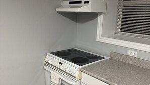 A kitchen with a white stove, oven, and countertop, a window with blinds, and a wooden floor. - Relaxing Lake Haven | Peaceful (Saint John)