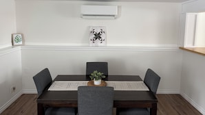 A dining area with a dark wooden table, grey upholstered chairs, a white wall-mounted air conditioner, and a framed artwork. - Relaxing Lake Haven | Peaceful (Saint John)