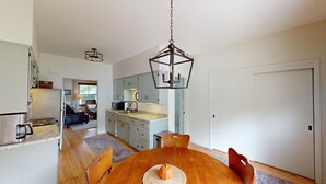 A modern kitchen with white cabinets, a wooden dining table, and a hanging light fixture.