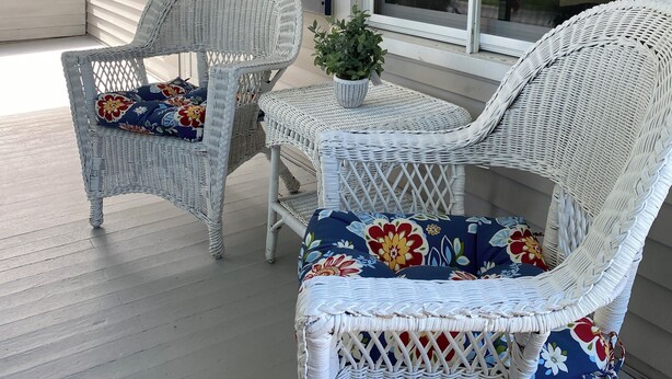 A porch with wicker furniture, including two chairs and a table, and a potted plant.