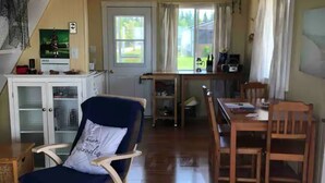 Un vaste espace de vie doté d’un plancher en bois, d’un fauteuil bleu, d’une table à manger avec des chaises, d’un coin cuisine et d’un escalier menant à un autre niveau.