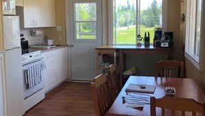 Une cuisine avec des meubles de rangement en bois, une cuisinière et un coin repas comprenant une table et des chaises.