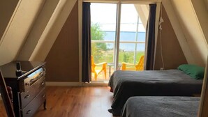 Une chambre avec deux lits, une commode et une vue sur la mer grâce à de grandes fenêtres.