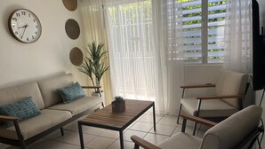 Ein Wohnzimmer mit einer Couch, zwei Sesseln, einem Couchtisch, einer Uhr und einer Pflanze.