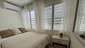 Ein Schlafzimmer mit einem Bett, einem Nachttisch, einer Zimmerpflanze und einem Fenster mit Jalousien.