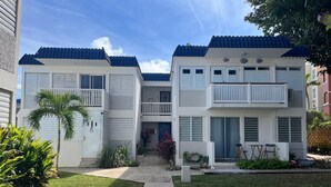 Ein zweigeschossiges Wohnhaus mit blau gefliestem Dach, weißer Fassade und einer kleinen Veranda mit einer Bank.