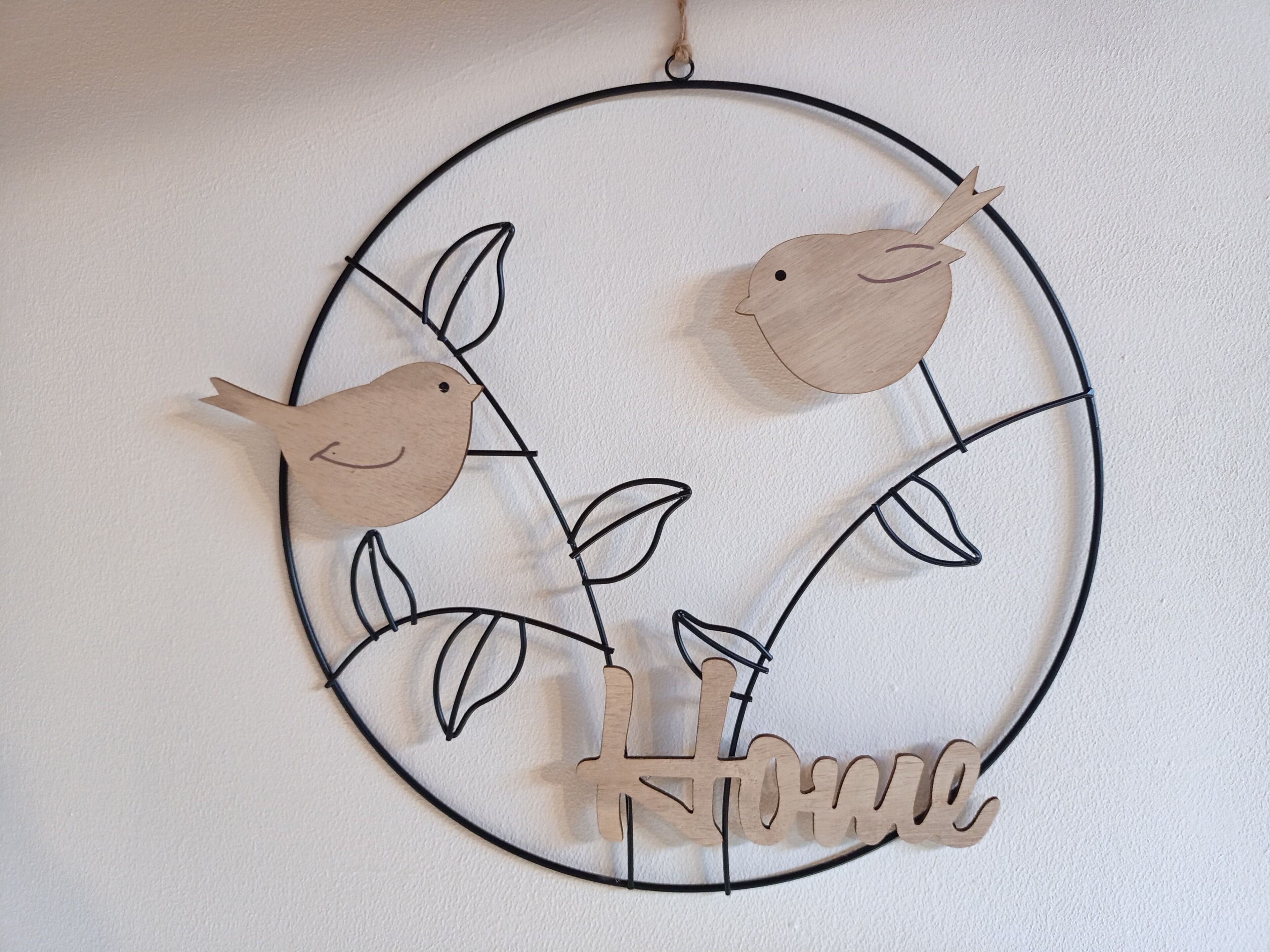A circular wall decoration with two wooden birds and the word "Home" at the bottom.