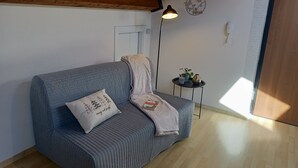 Una habitación acogedora con un sofá gris, una mesita auxiliar con lámpara y techo de madera.