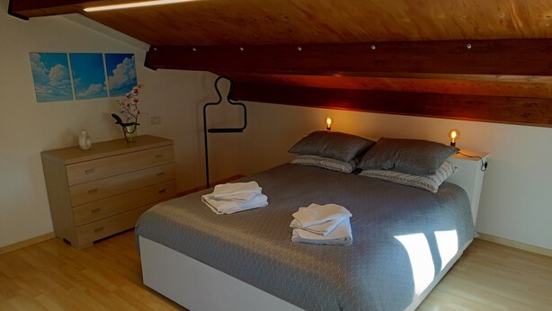 Un dormitorio con cama, dos lámparas de noche, cómoda y repisa con objetos decorativos.