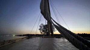 A cable-stayed bridge at dusk with a clear view of the moon in the sky.